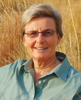 Woman with gray hair and glasses smiling for the camera in front of a straw field