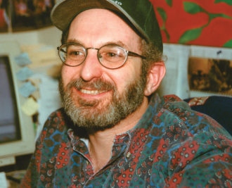 Man with hat and glasses smiles at something past the camera
