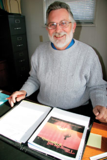 A man smiling in front of a copy of 'Tilling the Soil of Opportunity' with a pen in hand.