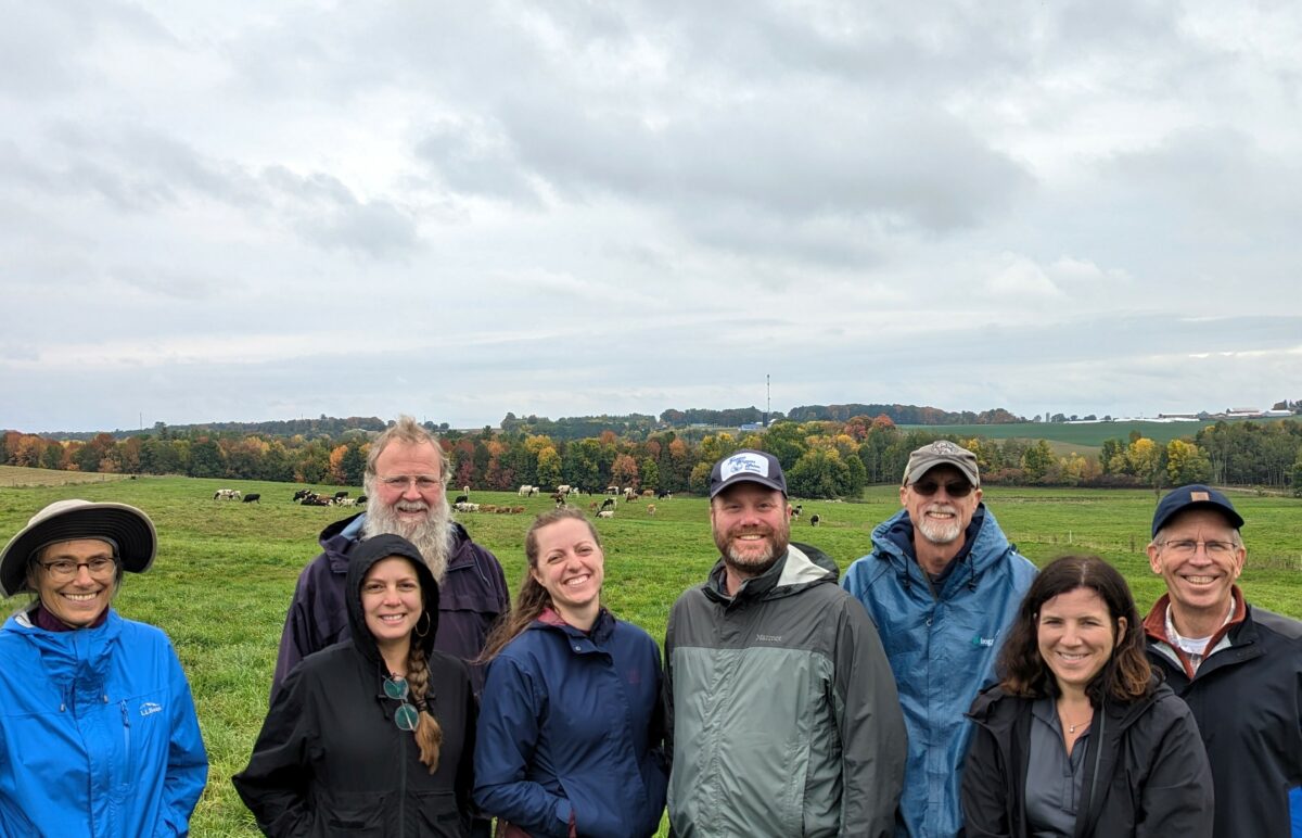 Eight people dressed for fall weather standing in a pasture looking directly at the camera.