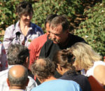 A man talks to a group of people looking down at something outside