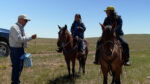 Rancher talks with two others on horseback in an open field.
