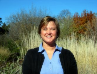 Beth Nelson standing for a headshot in front of wild grasses and autumn trees