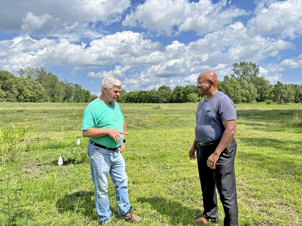 Two men standing in a green field talking to each other on a sunny day