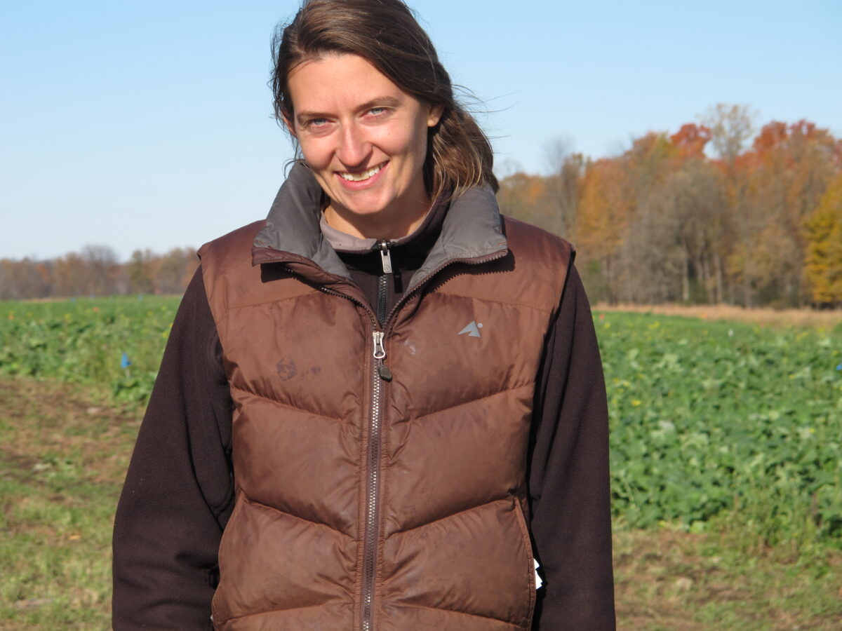 A person standing outside in a brown vest in front of a green field