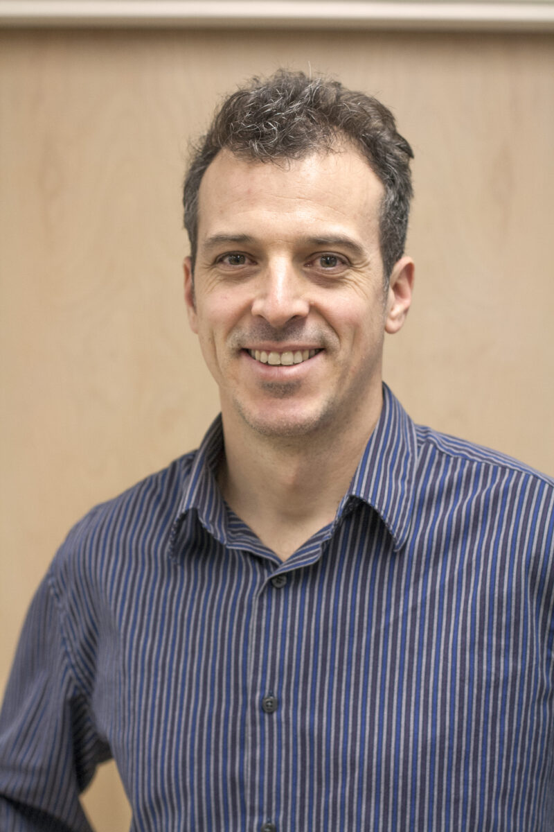 Headshot of a person in a blue collared striped shirt