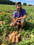 man kneeling down in a field next to a pile of harvested butternut squash