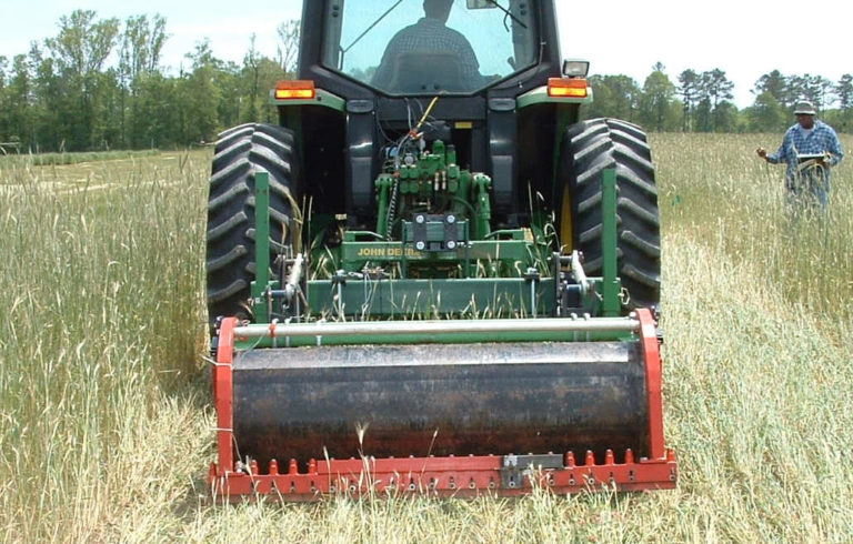 A tractor with a roller in the back in a field