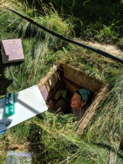 Women in a square hole in the ground looking up, while taking samples.