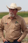 Rancher in a brimmed hat and a brown button down in front of a field