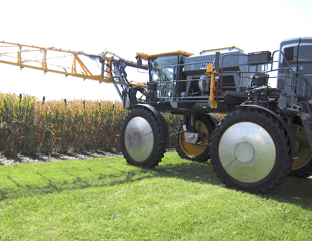 A high clearance seeder mounted on a tractor is preparing to enter a field of corn prior to corn harvest