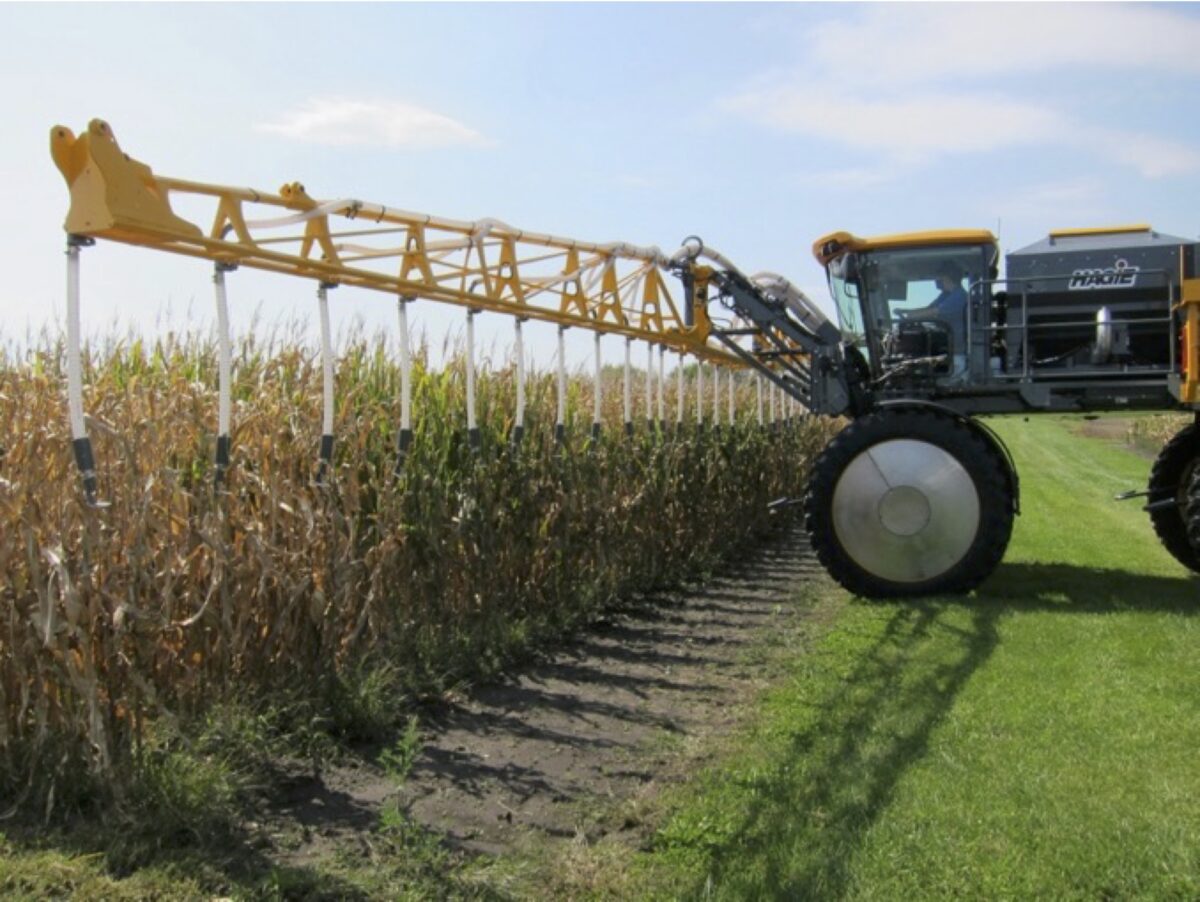 a tractor with a large interseeder mounted on the front sits next to a field of late season corn