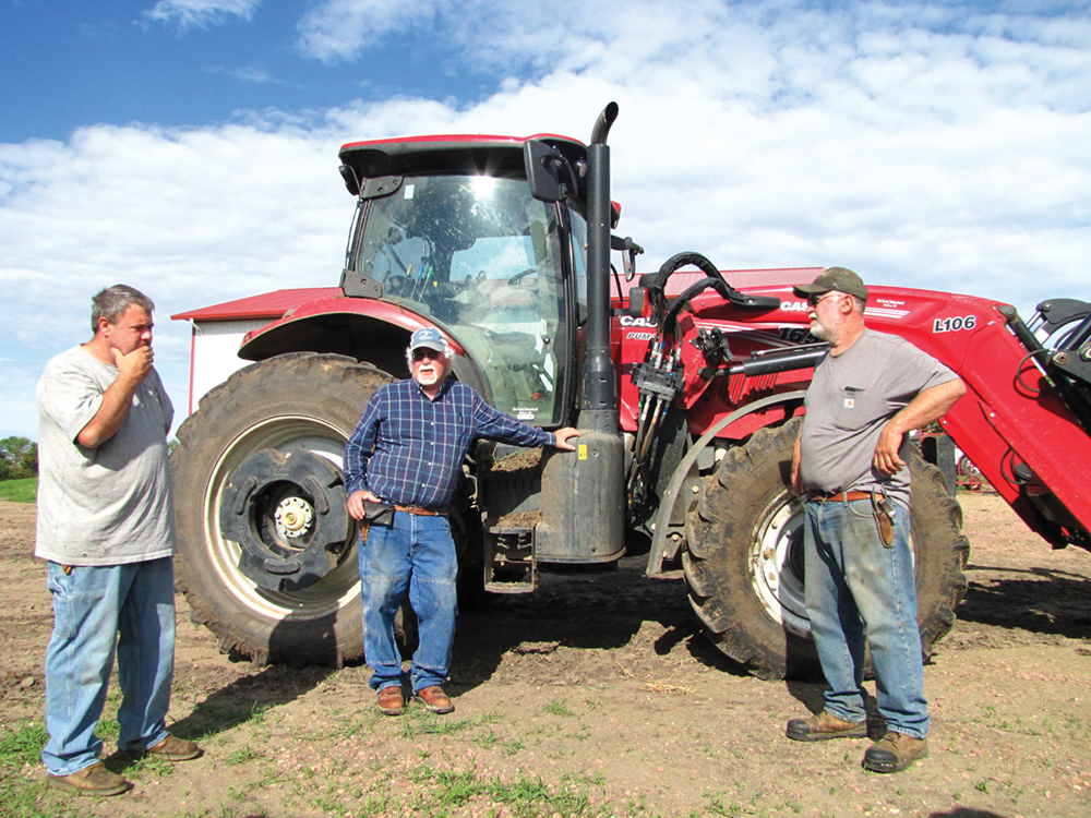 Three brothers standing in front of a tractor discussing their daily plans.