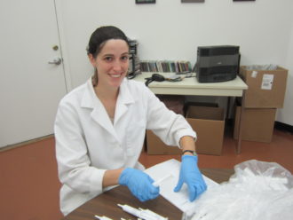 Keena Mullen working in a lab with a white coat and blue surgical gloves