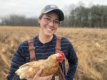 photo of woman wearing a brimmed basebell hat and glasses holding a chicken