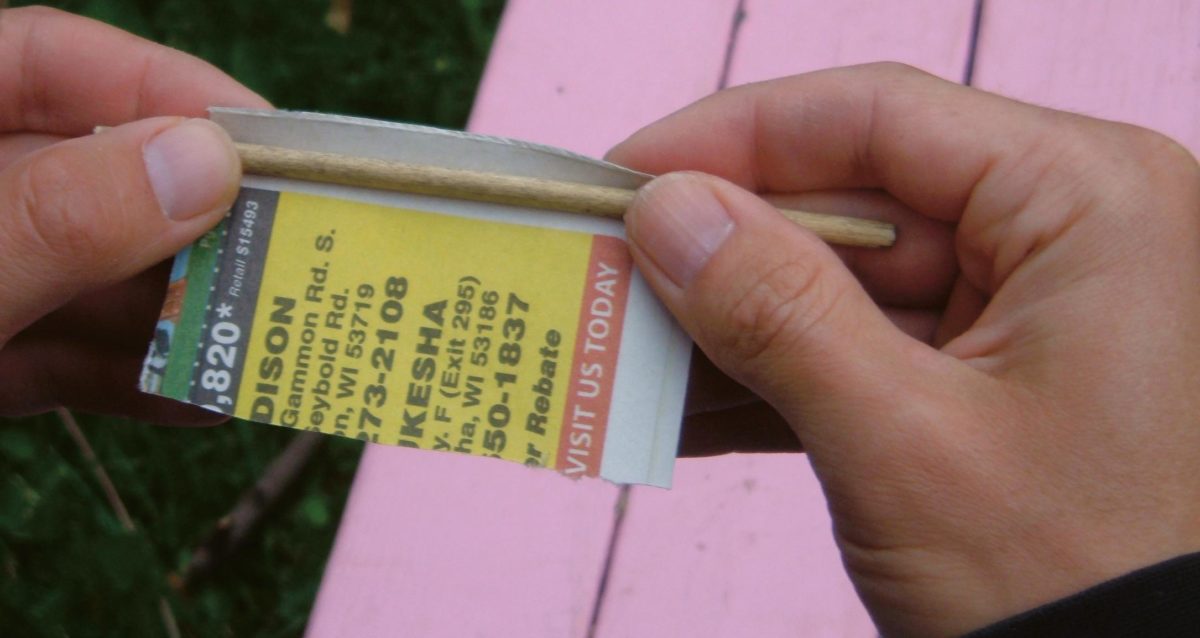 Paper being wrapped around a wooden dowel to make a paper tube liner.