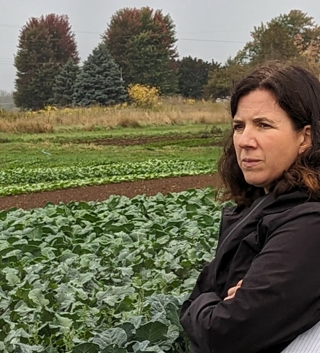 A woman in a black coat standing in a row of mixed vegetable crops.
