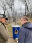 Two men talking to each other outside in front of a blue can.