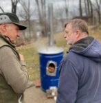 Two men talking to each other outside in front of a blue can.