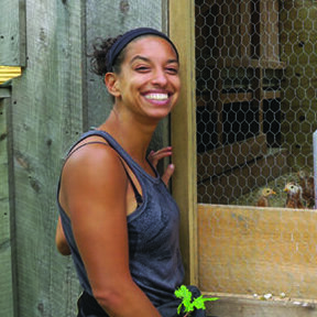 A young Black woman posing at her chicken coop