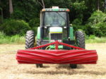 Red roller crimper attachment to a green tractor