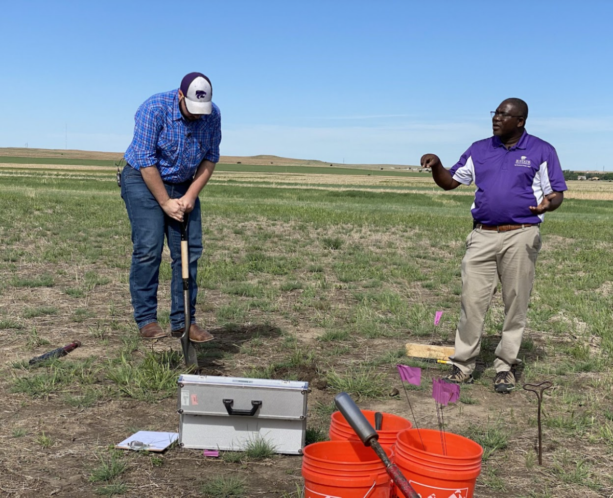 Two people standing in a field talking, with farming tools in front of them