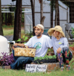 Two people sitting in a grass field with baskets and hats outside