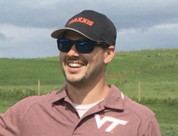 A man in a VT polo, hat, and sunglasses smiling into the distance