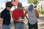 Three people standing outside looking at papers that the middle person holds