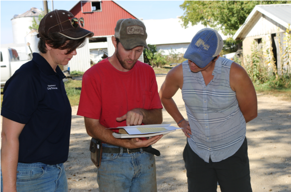 Three people standing outside looking at papers that the middle person holds