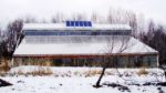 Snowy building with solar panels on the roof and winter trees behind.