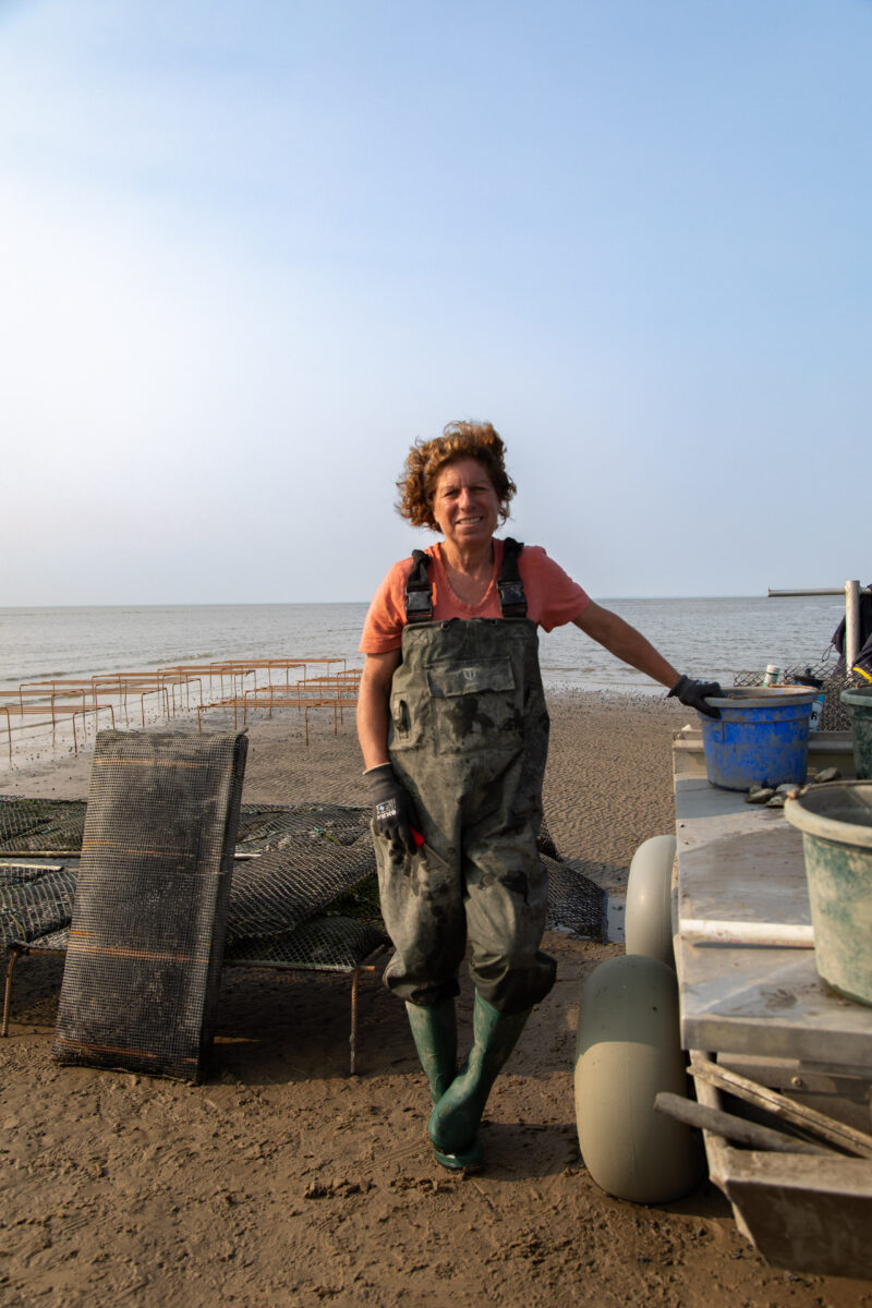 A woman standing by the bay in overalls holding a blue bucket