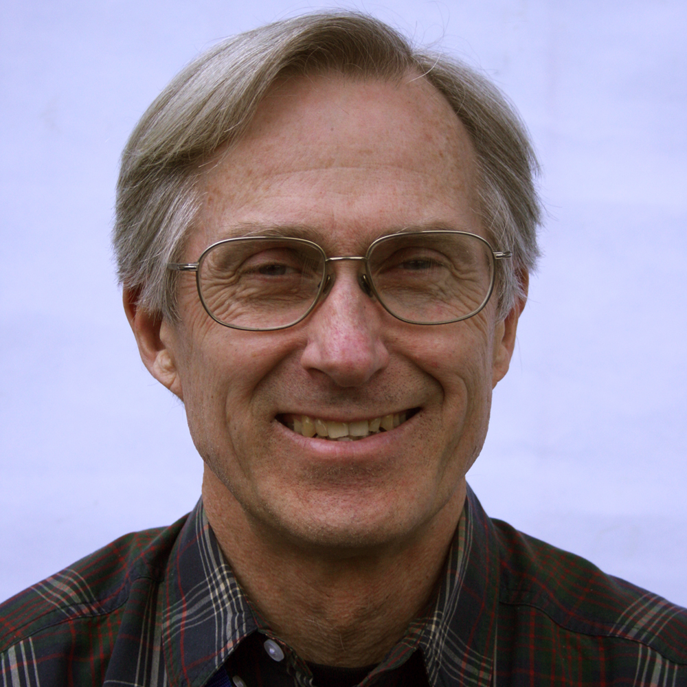 A man with gray hair and glasses smiling at the camera