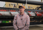 A man in a baseball cap sitting in a machine shed.