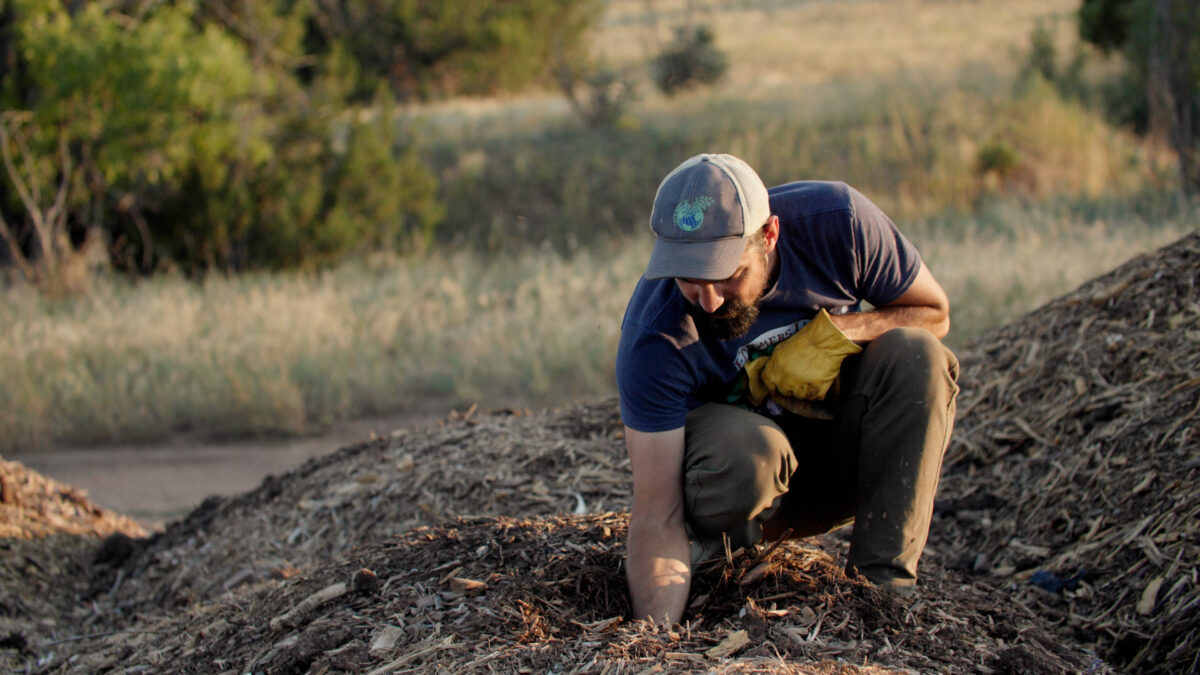 a rancher kneeling and inspecting a compost pile