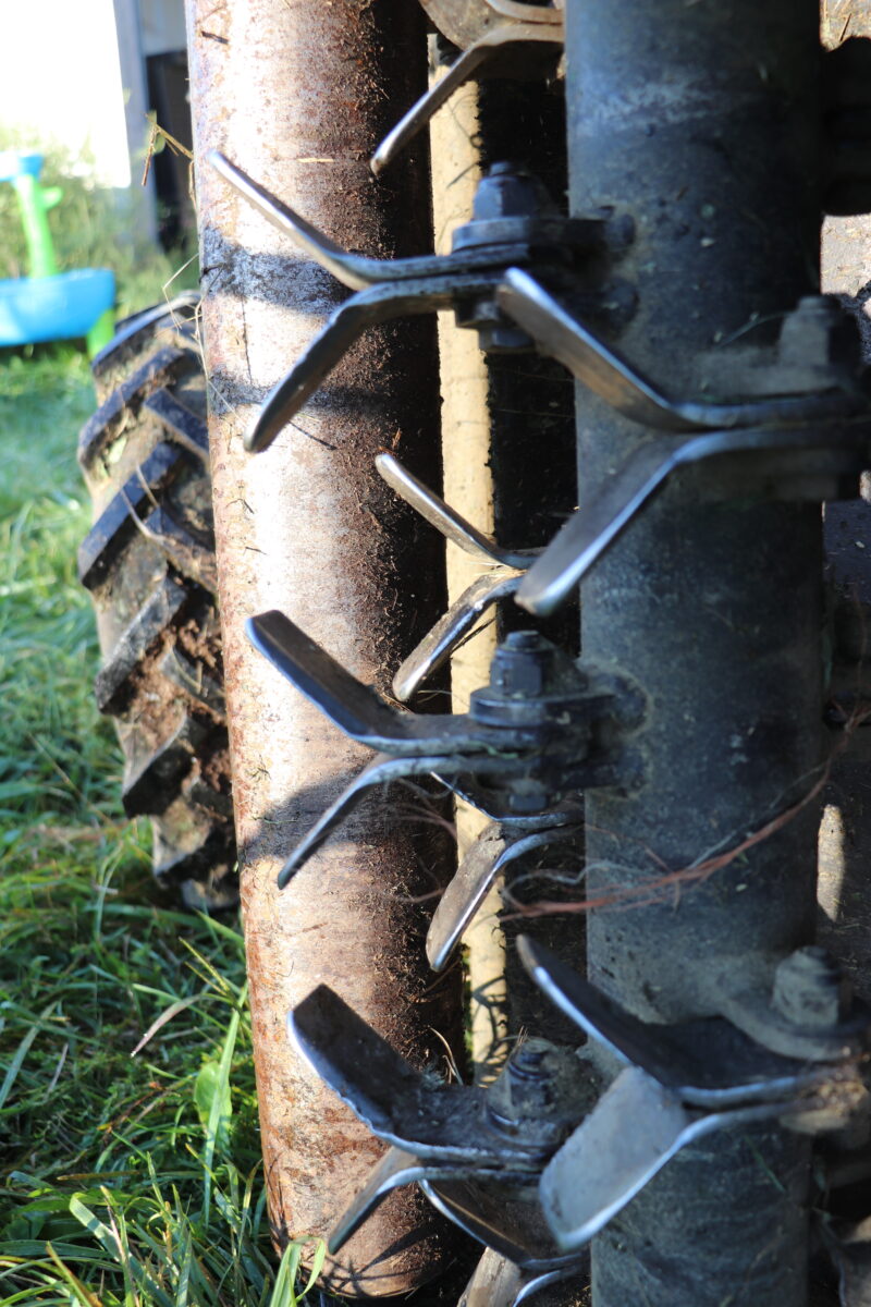 a flail mower has been turned on its side to show a close up view of its blades, specifically how they have been set low to the ground