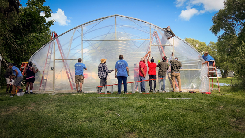 volunteers working together to add plastic sheeting to a new high tunnel