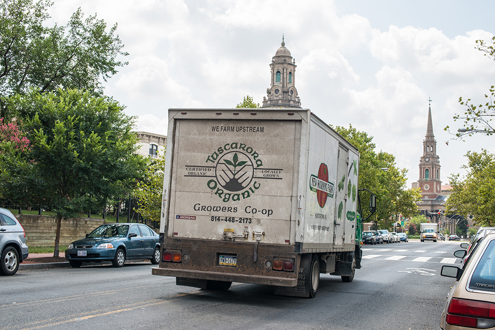 A delivery truck branded with a farm coop drives down a city street.