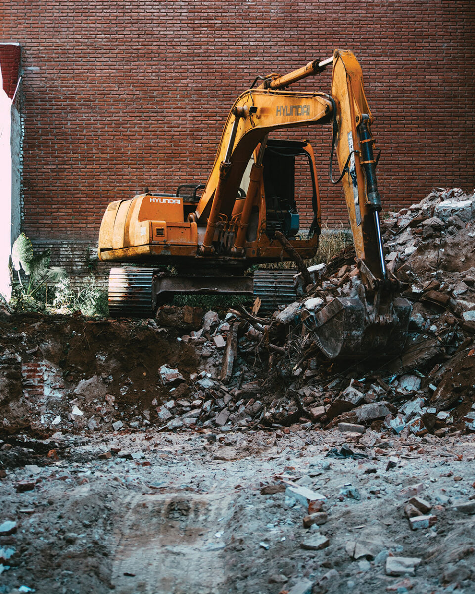 Yellow excavator scooping out rubble in an alley way
