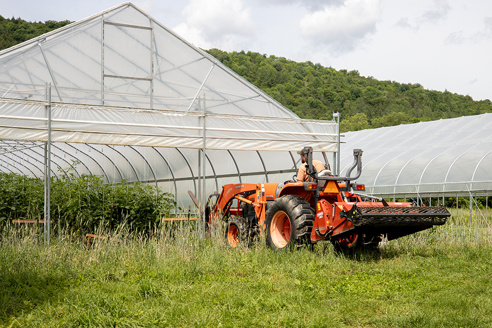 A farmer drives a tractor inside a high tunnel.