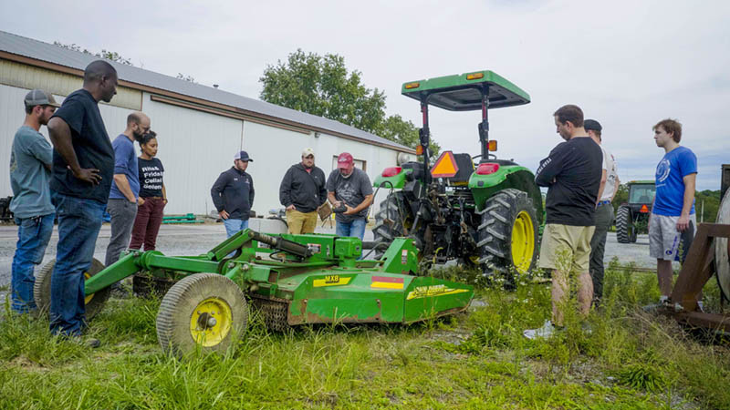 Students gathered around a tractor and mower are learning about equipment safety