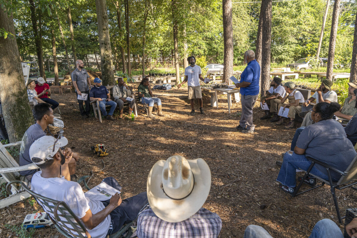 wo people standing and talking in a circle surrounded by seated farmers