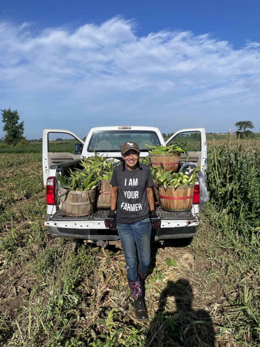 A farmer poses in the tailgate of a truck in a farm field. 