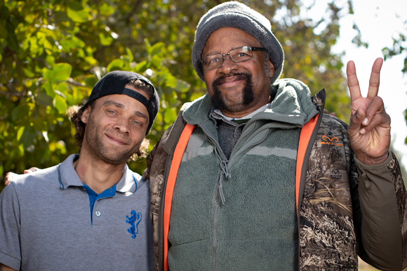 A farmer posing with his adult son and giving the peace sign