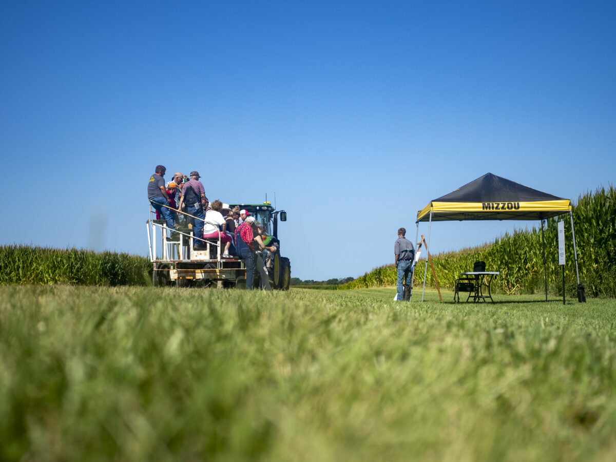 People sitting in the back of a tractor listening to a speaker