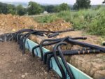 Multiple black pipes coming out of the ground at the edge of a hole. They are being buried for geothermal heat