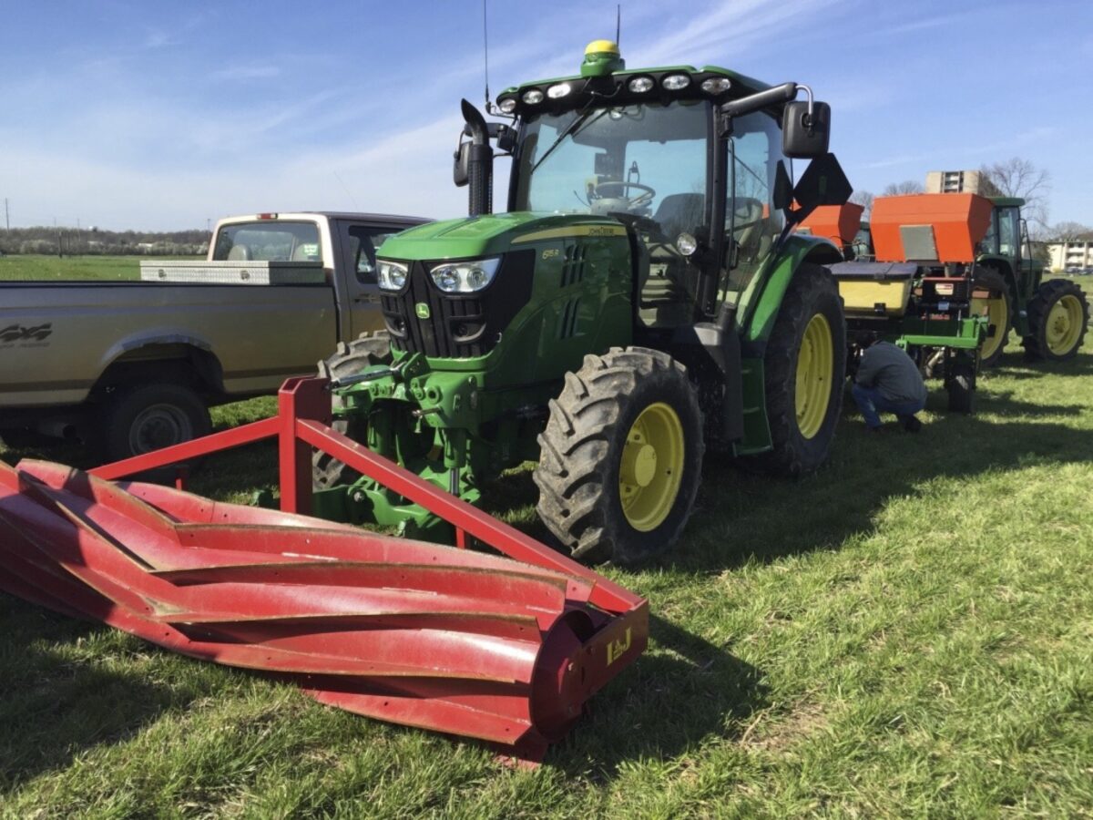 A roller crimper is mounted to the front of a tractor that is sitting unused in a field