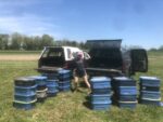 A famer flexing their arms as a display of strength in front of trucks being loaded with soil samples