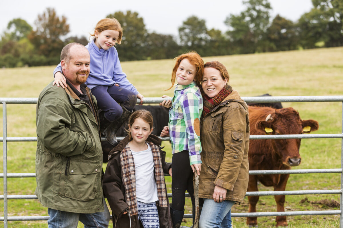 A family of 5 in front of a horse and a fence in a field