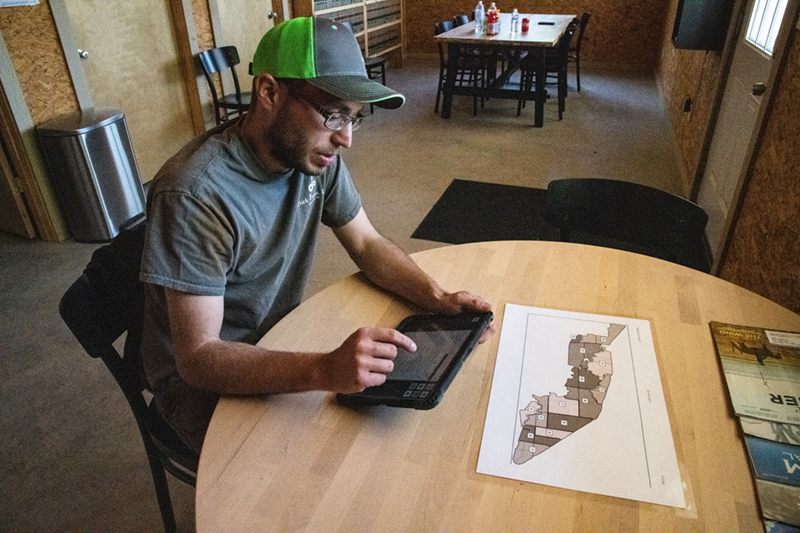 A young farmer at the kitchen table with a tablet and paper field maps